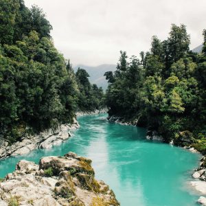 Beautiful turquoise river winding through a dense, lush forest under a cloudy sky.